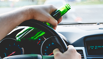 A driver holds a beer bottle in one hand